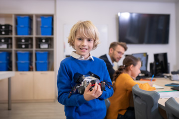 Boy holding buildable car, teacher and girl sitting at desk