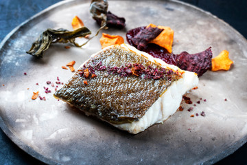 Gourmet fried European skrei cod fish filet with algae and vegetable crisps as closeup on a modern...