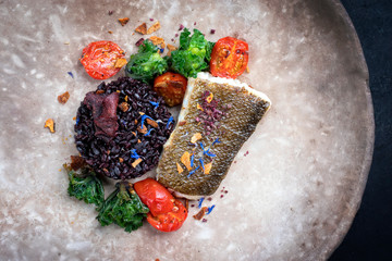 Gourmet fried European skrei cod fish filet with kalette and black venus rice as top view on a modern design plate
