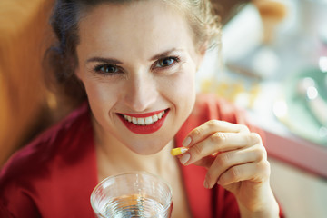 woman with cup of water taking pill at modern home in sunny day