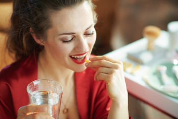 happy 40 years old housewife with cup of water taking pill