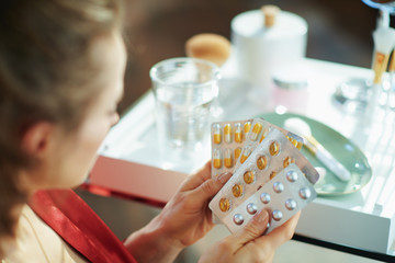 woman holding blisters with pills in modern house in sunny day