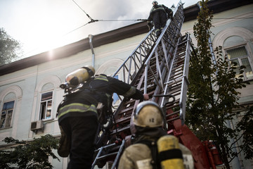 Firefighters on ladders in oxygen masks extinguish the fire in an old house in the middle of the city