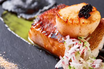 Scallops and ravioli. Seafood, pike perch fish, caviar and black dumplings in a plate on a dark table close-up. Healthy food.