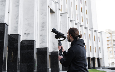 Young Professional videographer holding professional camera on 3-axis gimbal stabilizer. Pro equipment helps to make high quality video without shaking. Cameraman wearing black hoodie making a videos. © Volodymyr_sh