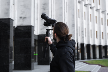 Young Professional videographer holding professional camera on 3-axis gimbal stabilizer. Pro equipment helps to make high quality video without shaking. Cameraman wearing black hoodie making a videos. © Volodymyr_sh