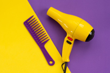 Beauty topic: Yellow hair dryer and stylist's comb over purple background. Fashion and style concept.