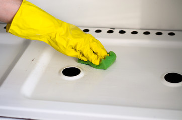 A girl in yellow gloves washes a gas stove.