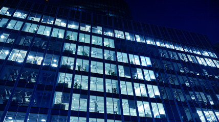 Fototapeta na wymiar Night architecture - building with glass facade.Blue color of night lights. Modern building in business district. Concept of economics, financial. Photo of commercial office building exterior. Abstra