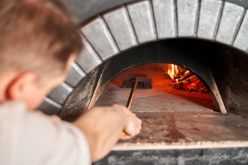 Pizza Chef cleaning pizza oven with special brush. Traditional wood oven in restaurant, Italy. Original neapolitan pizza. Red hot coal.