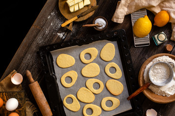 Fototapeta na wymiar overhead shot of baked egg shaped easter cookies on baking tray on rustic wooden table with flour, eggs, butter, lemon. process of baking cookies. easter card