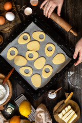 overhead shot of baked egg shaped easter cookies on baking tray on rustic wooden table with flour, eggs, butter, lemon. process of baking cookies. easter card