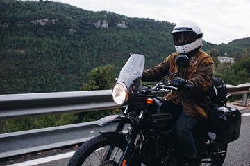 Man on modern and expensive touring motorcycle rides on cloudy day on mountain road. Motorcycle driving conept in fullface helmet for safety