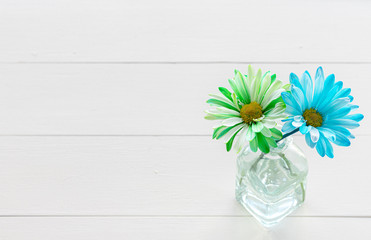 Green and Blue Daisies in Vase on White Wood Table