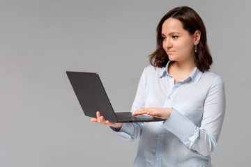 Charming young woman working freelance, remote from office, hold laptop, typing university essay, turn left smiling copy space, stand gray background joyful, browsing web using computer