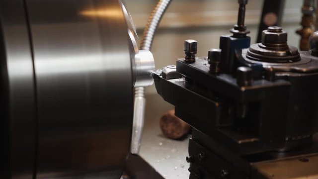 Turning bench lathe machine working on a metal rod piece casting metal shavings - closeup on the cutting edge and workpiece