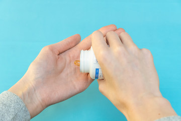 One hand pours yellow vitamin capsules into the other hand on a blue background