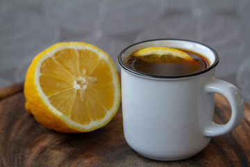 A cup of black coffee with a slice of lemon on a grey tablecloth, selective focus
