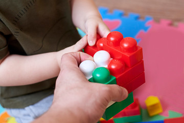 Hands of dad and son playing with a colorful constructor set.