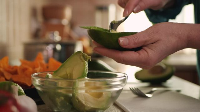Making guacamole for a tortilla chips snack - closeup on hands scooping avocado into bowl, camera orbit around