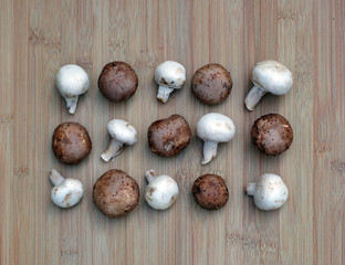 Arrangement of raw white champignons and brown crimini mushrooms on a bamboo board