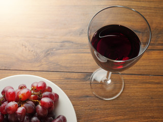 Fresh red grapes on a white plate and a glass of a red wine on a wooden table.