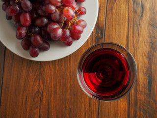 Fresh red grapes on a white plate and a glass of a red wine on a wooden table.