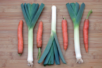 An arrangement with alternating positions of raw leeks and carrots on a bamboo board
