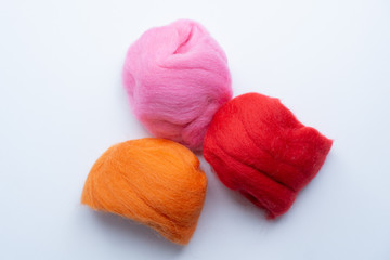 Top view of three pieces of orange, pink and red wool on white background. Concept of felting creative hobby.