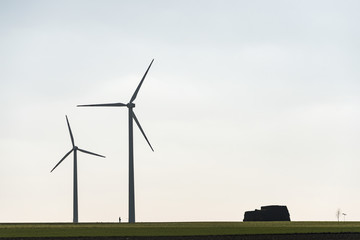 Fototapeta premium Two wind farms and a human silhouette showing the scale of these objects. All on the background of blue sky and green field.