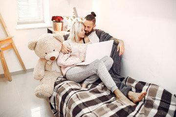 Cute couple in a bedroom. Lady in a pink sweater. Pair at home use a laptop