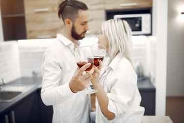 Cute couple in a kitchen. Lady in a white t-shirt. Pair at home drinking a vine.