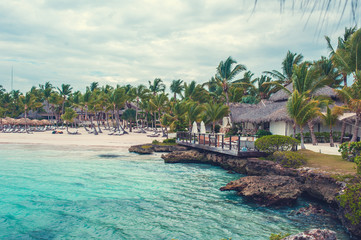Tropical beach with rocks and coconut palm trees, color toned picture
