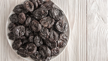 Prunes in a white ceramic plate on a light wooden rustic table.