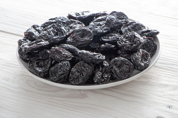 Prunes in a white ceramic plate on a light wooden rustic table.