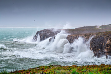 A huge ocean waves breaking on the coastal cliffs in at the cloudy stormy day. Breathtaking romantic seascape of ocean coastline.