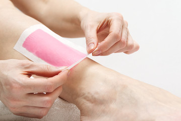 Woman using pink wax strips. Beautiful woman doing depilation for her legs with waxing, isolated on white