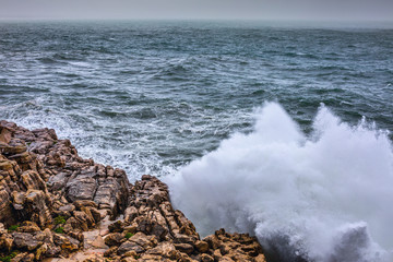 A huge ocean waves breaking on the coastal cliffs in at the cloudy stormy day. Breathtaking romantic seascape of ocean coastline.
