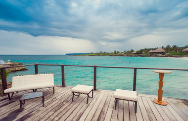 Fototapeta na wymiar Outdoor terrace with Empty wooden table and chair with Sea view of Indain ocean, Maldives background. Chairs, table and sofa at the Terrace with panorama view of sea.