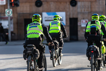 Four cyclist police officers are seen from the rear, wearing high visibility vest and safety...
