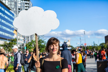 A close up head shot of a young woman holding a cloud shaped blank protest placard at a climate...
