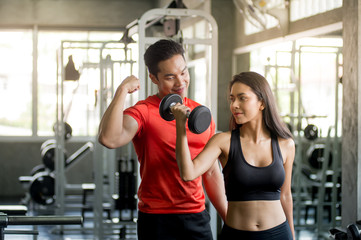 Fototapeta premium The interesting male trainer teaches how to give dumbbells to attractive women and smiley faces in the gym.