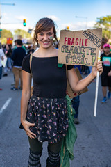 A close up view of a happy blonde woman during a climate rally, holding a cardboard sign saying...