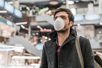 Young man in protective face mask at shopping mall. Air pollution, virus and health concept