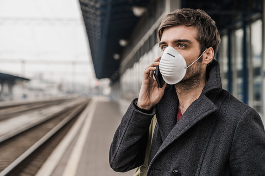 Young caucasian male in protective mask talking on his mobile phone on train station