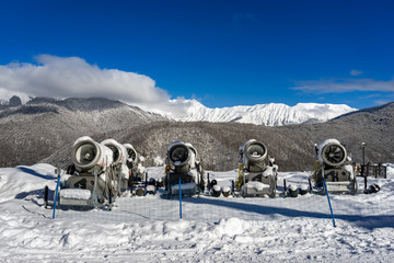 Snow machine guns, standing in row on the slope of ski resort against the background of landscape...