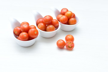 Fresh cherry tomato, displayed in containers on white wooden background