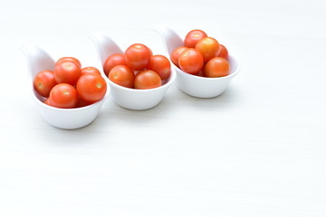 Fresh cherry tomato, displayed in containers on white wooden background