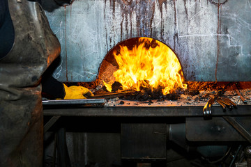 female metal artist pulls a workpiece from a blacksmith's furnace