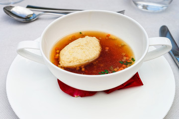 Closeup of beef broth with bread dumpling on white cup and plate
